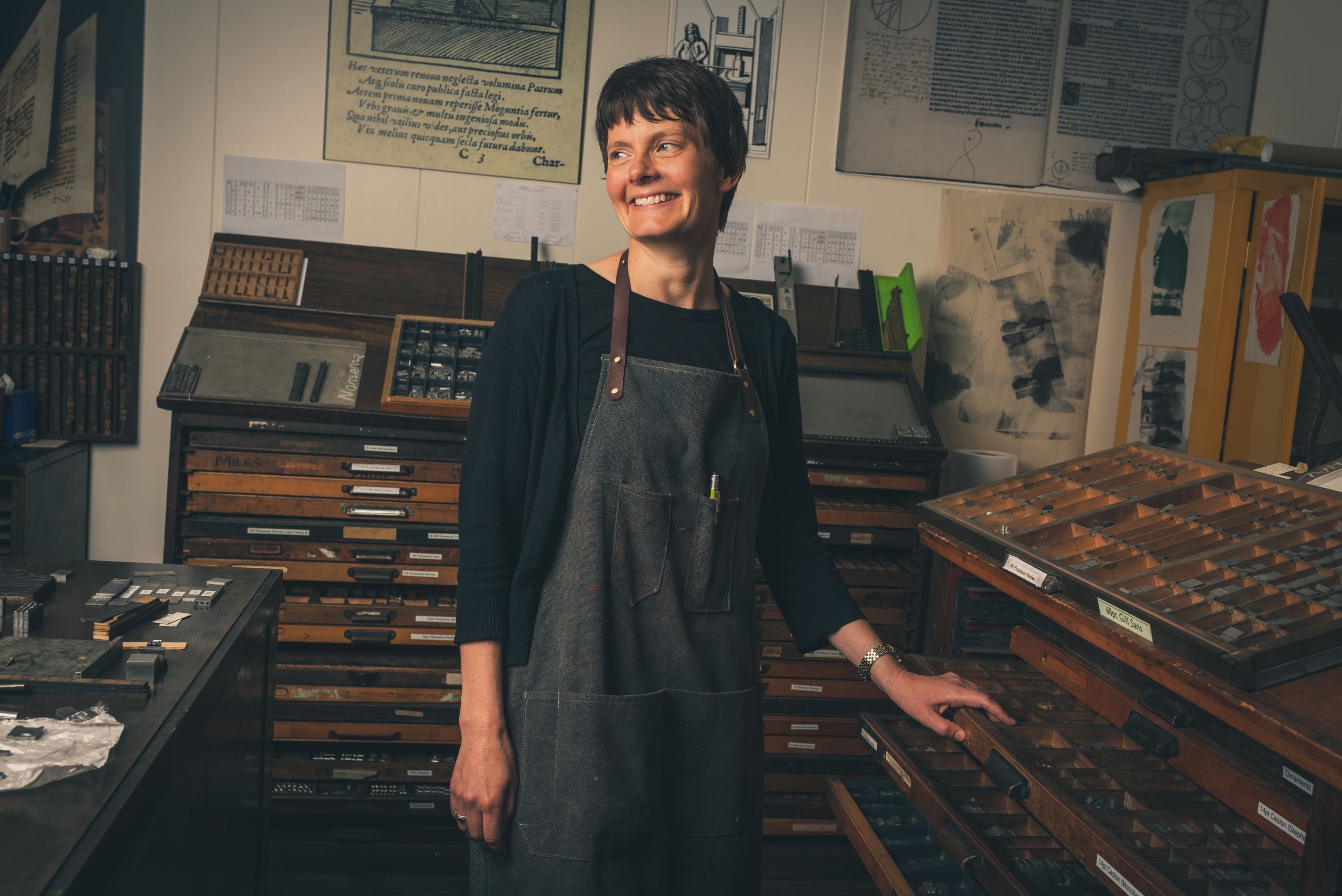 A lecturer from the Department of English stands next to a letterpress in the Thin Ice printing studio