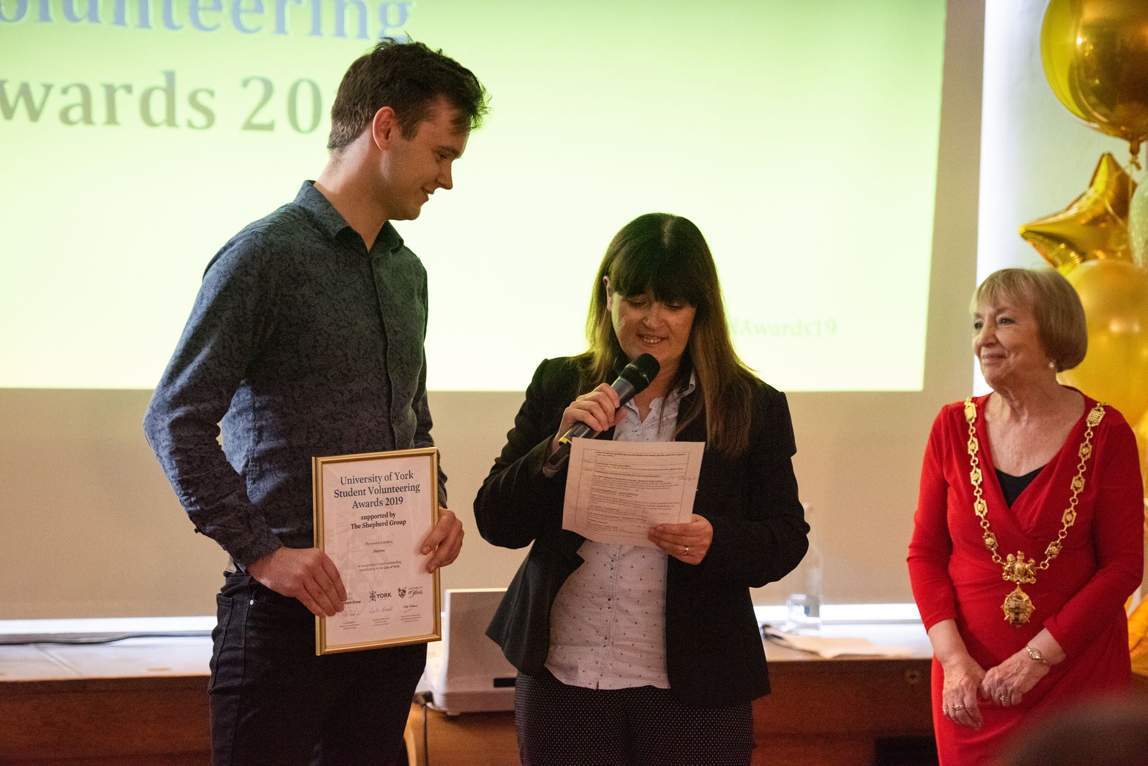 A student holds a volunteering award, watched by organisers of the University Volunteering Awards